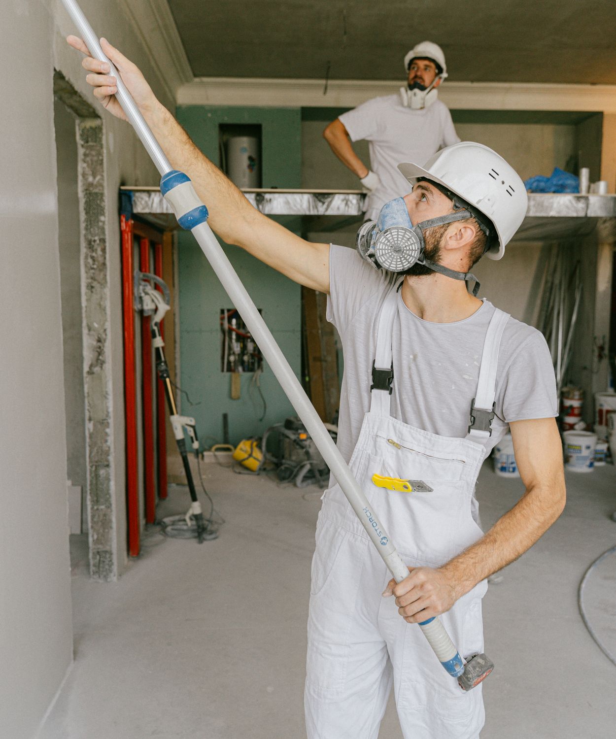 Profissional de obra com capacete e máscara aplicando massa em parede